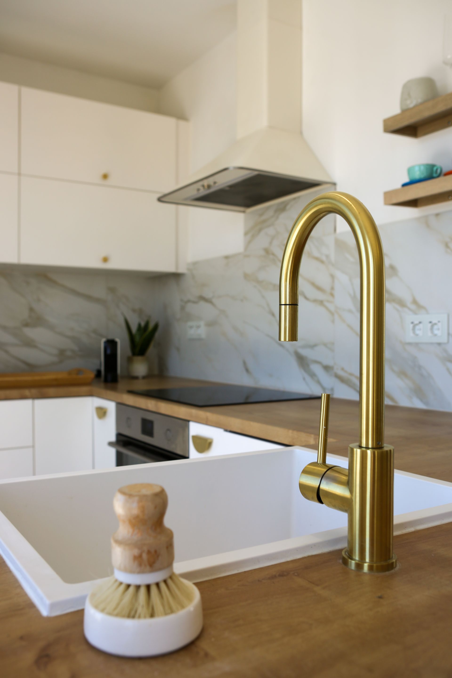 Gold faucet over a white sink in a modern kitchen with wooden countertops and white cabinets.