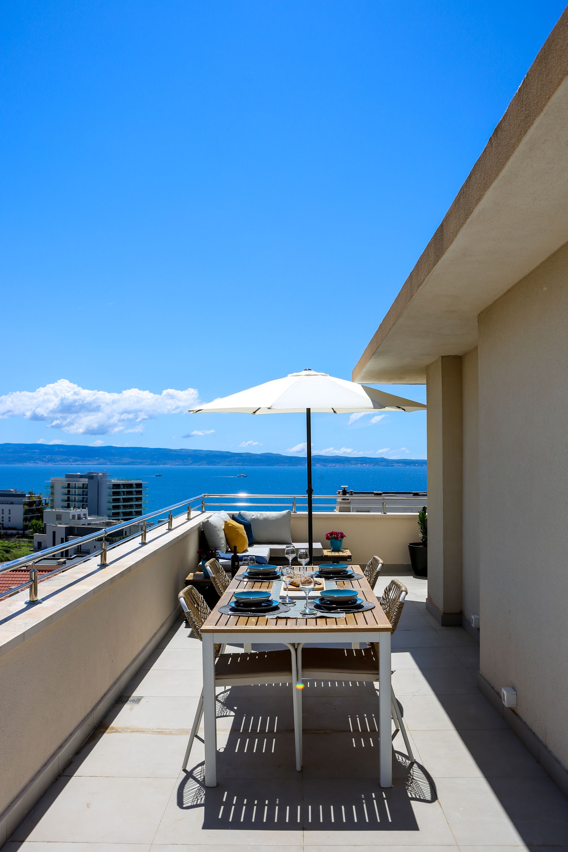 Rooftop patio dining table with umbrella overlooking the sea on a bright, sunny day.