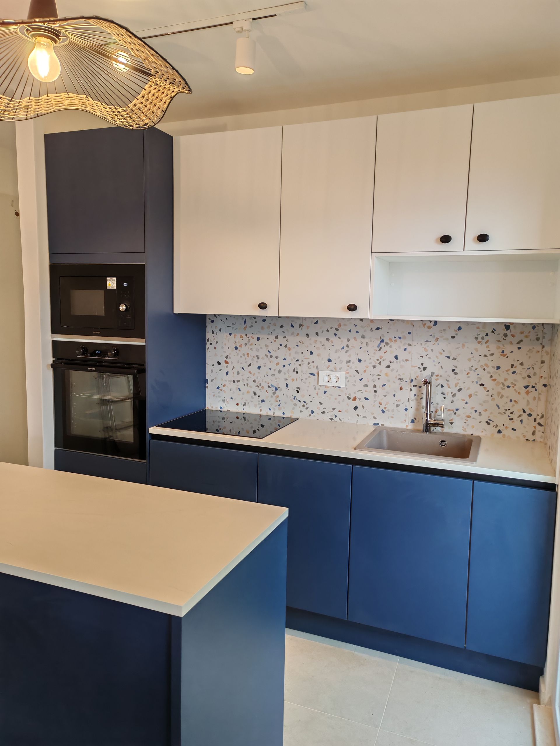 Modern blue and white kitchen with island, built-in appliances, and terrazzo backsplash.