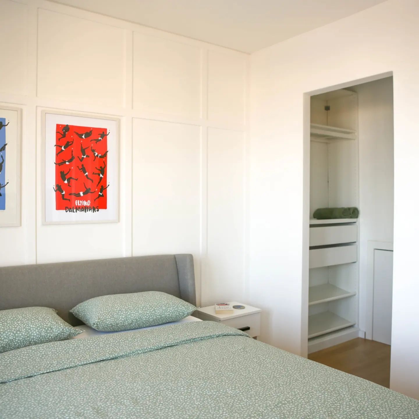 Bedroom with bed, closet, art, and white paneling.