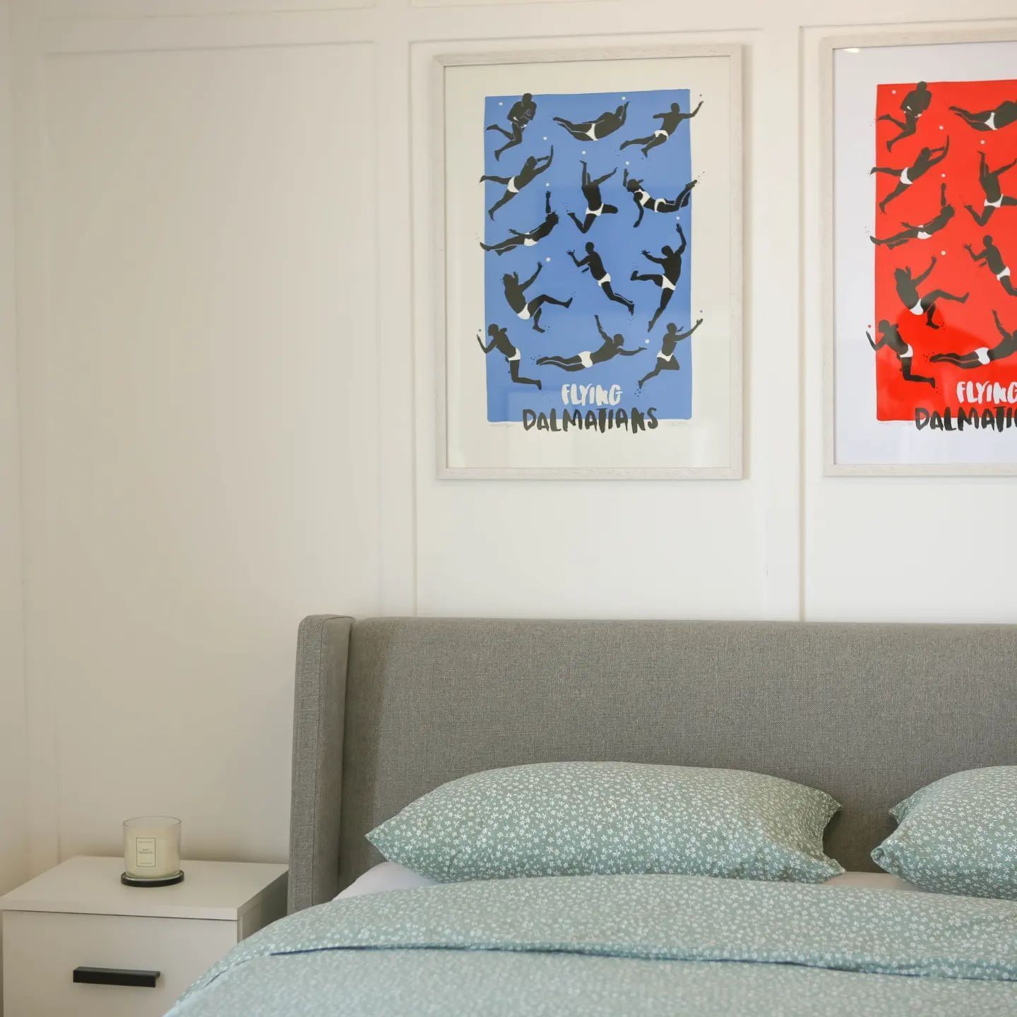 Bedroom with bed, nightstand, and framed prints of blue and red falling figures.