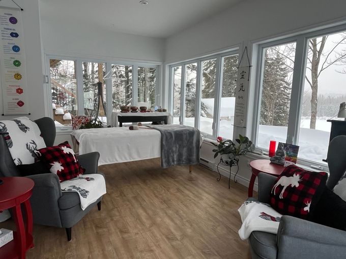 Salle de spa confortable avec table de massage, fauteuils et vue sur la neige à travers de grandes fenêtres.