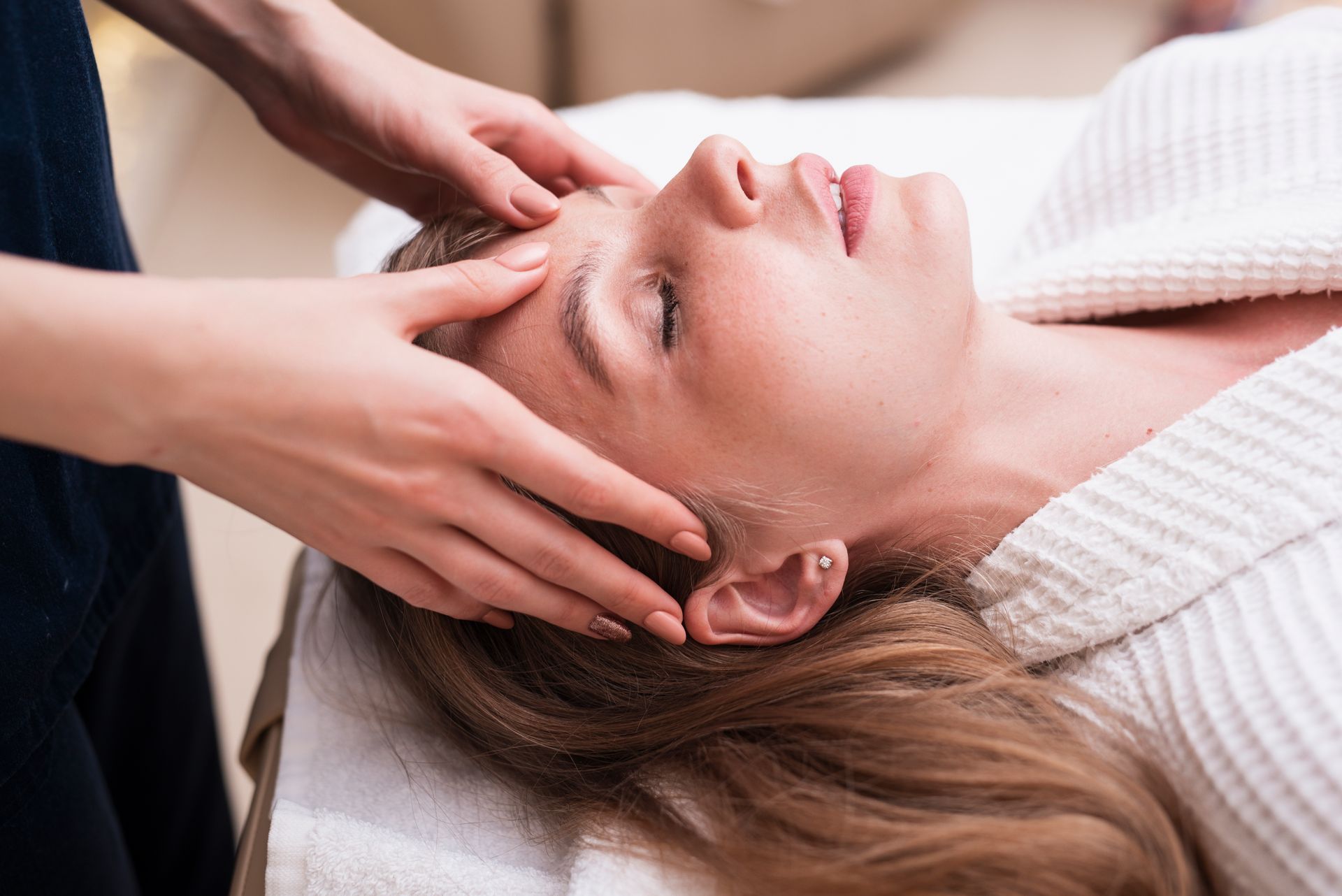 Une femme reçoit un massage de la tête dans un spa, les yeux fermés.