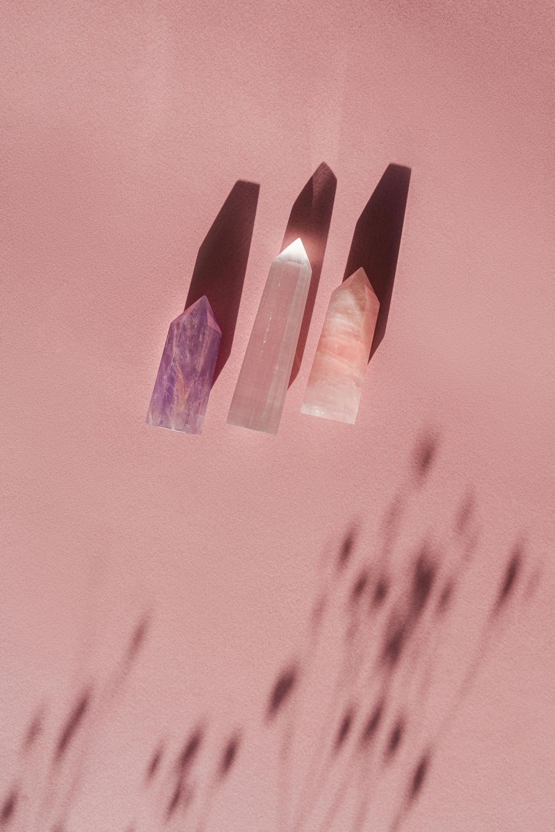 Trois cristaux projettent des ombres sur une surface rose.