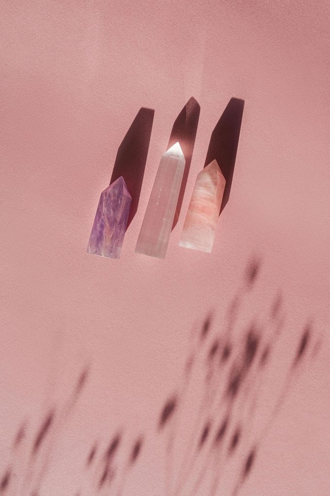 Trois cristaux projettent des ombres sur une surface rose.