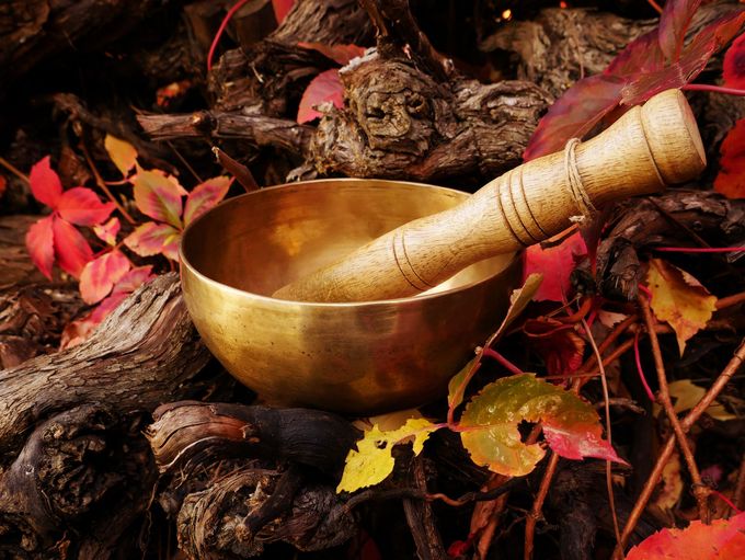 Bol chantant doré avec maillet en bois sur un lit de feuilles et de bois sombre.