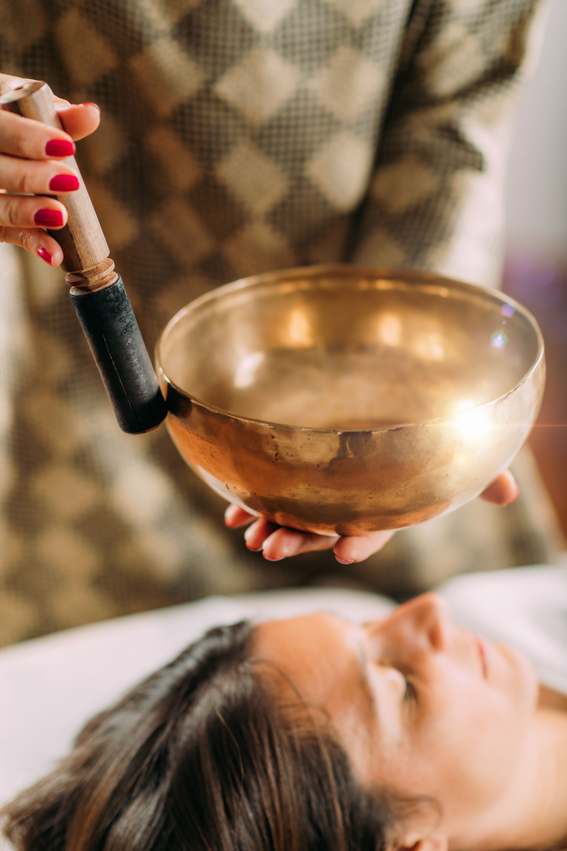 Une personne tient un bol chantant au-dessus de la tête d'une autre personne allongée, possiblement dans un spa.