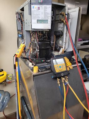 Technician working on an open HVAC unit with tools and a multimeter in a utility area