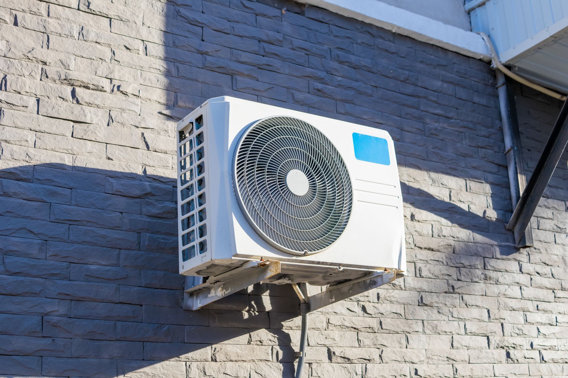 Outdoor wall-mounted air conditioner unit on a brick building wall, with a circular fan grille.