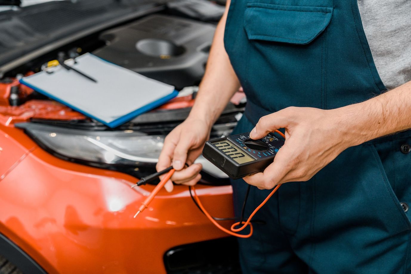 Meccanico che usa un multimetro per diagnosticare il motore di un’auto rossa in un’officina