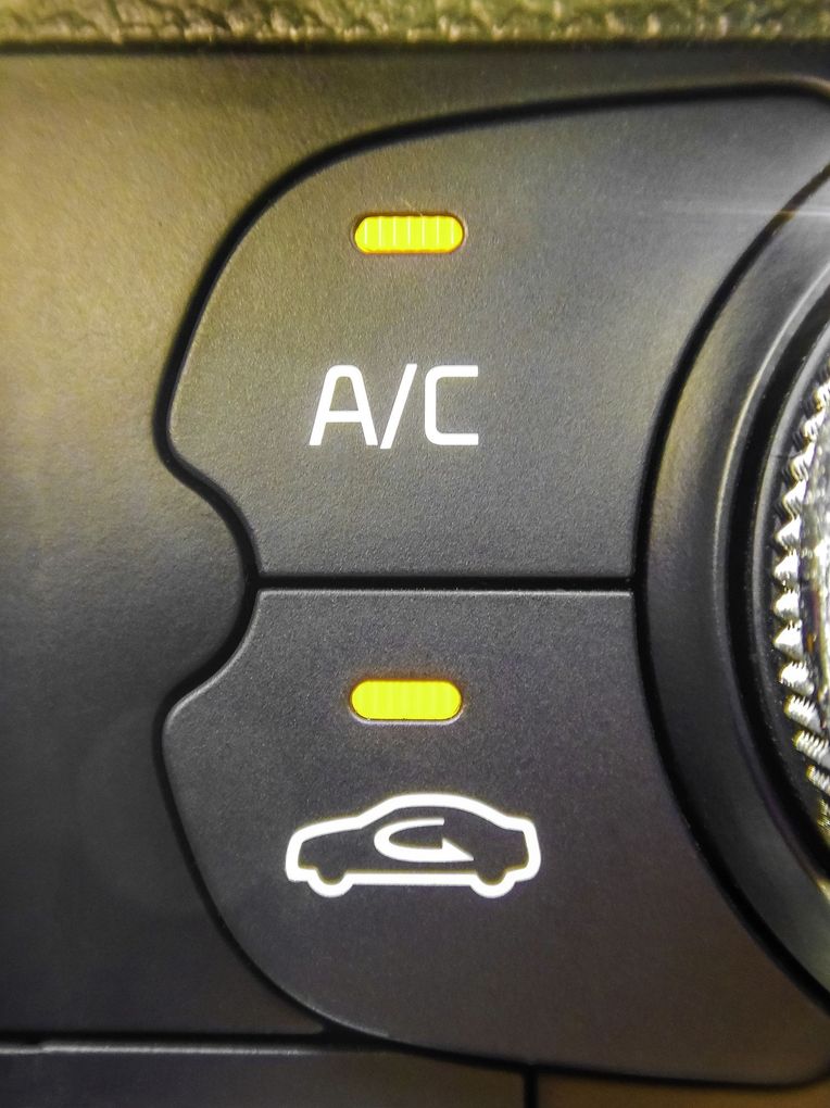 Pannello di controllo del climatizzatore dell’auto con i pulsanti A/C e ricircolo illuminati accanto a una manopola