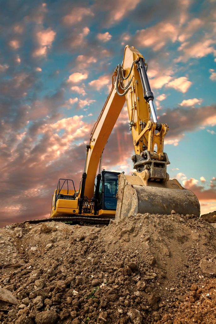 Escavatore giallo che scava nella terra in un cantiere, sotto un cielo nuvoloso al tramonto