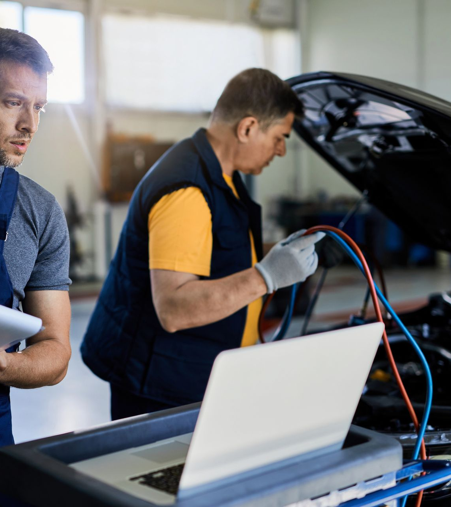 Meccanico che diagnostica il motore di un’auto con un laptop e dei cavi in officina