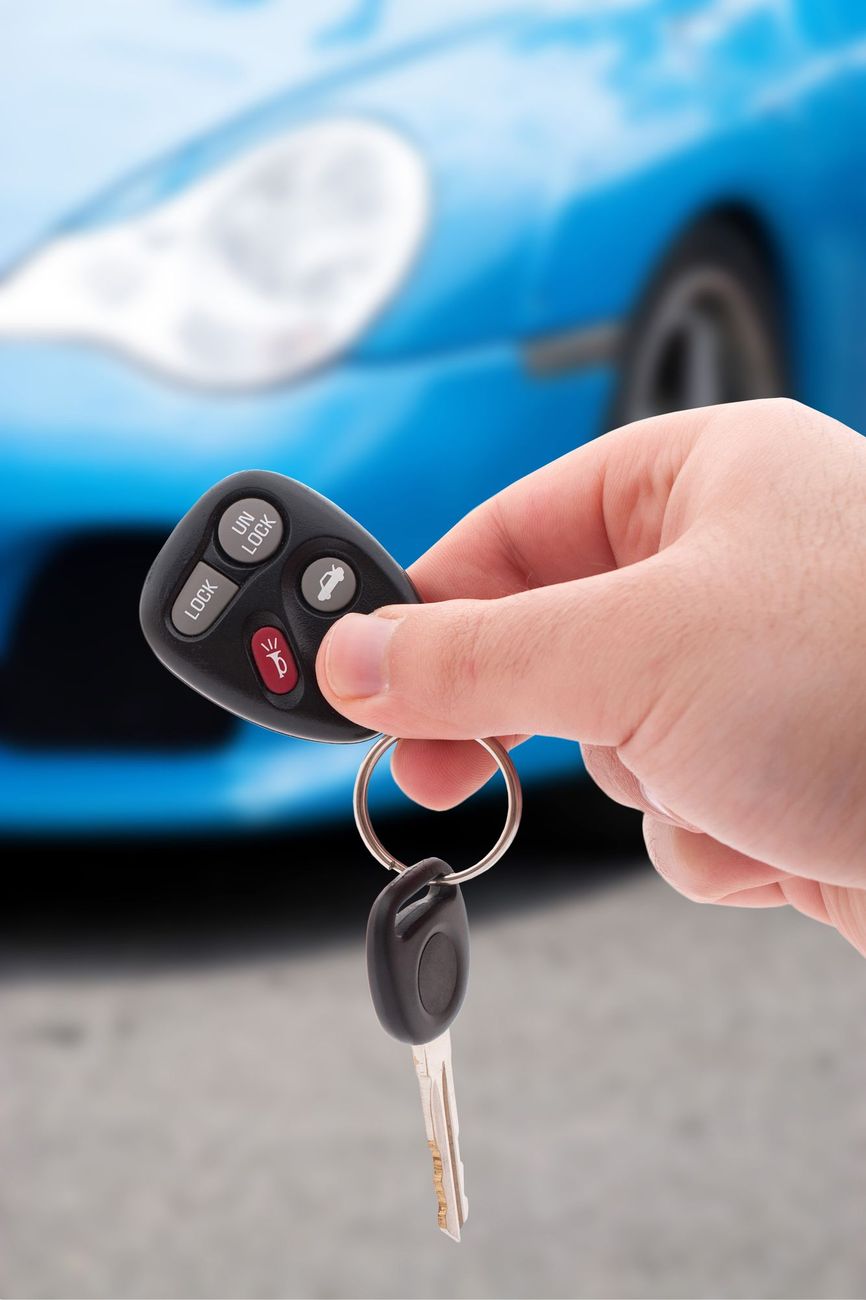 Mano che tiene un telecomando e una chiave davanti a un’auto blu