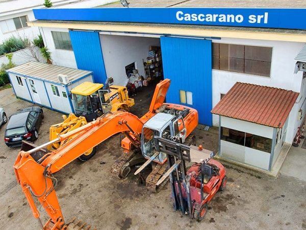 Macchinari pesanti parcheggiati all’esterno del magazzino di Cascarano srl, tra cui un escavatore arancione e altre attrezzature