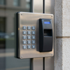 Wall-mounted keypad access control panel with fingerprint scanner and metal faceplate beside a doorway