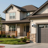 Two-story beige house with a front porch, stone accents, and a gray garage door