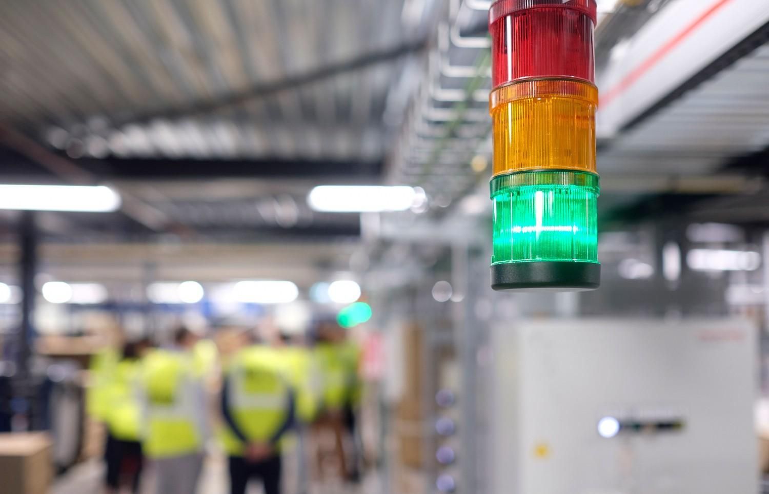 Red, yellow, and green stack light glowing in a factory with blurred workers in the background