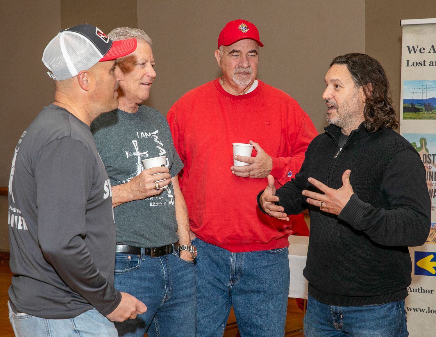 Three people chatting with Keith Nester at an indoor event, holding cups and wearing casual clothes.