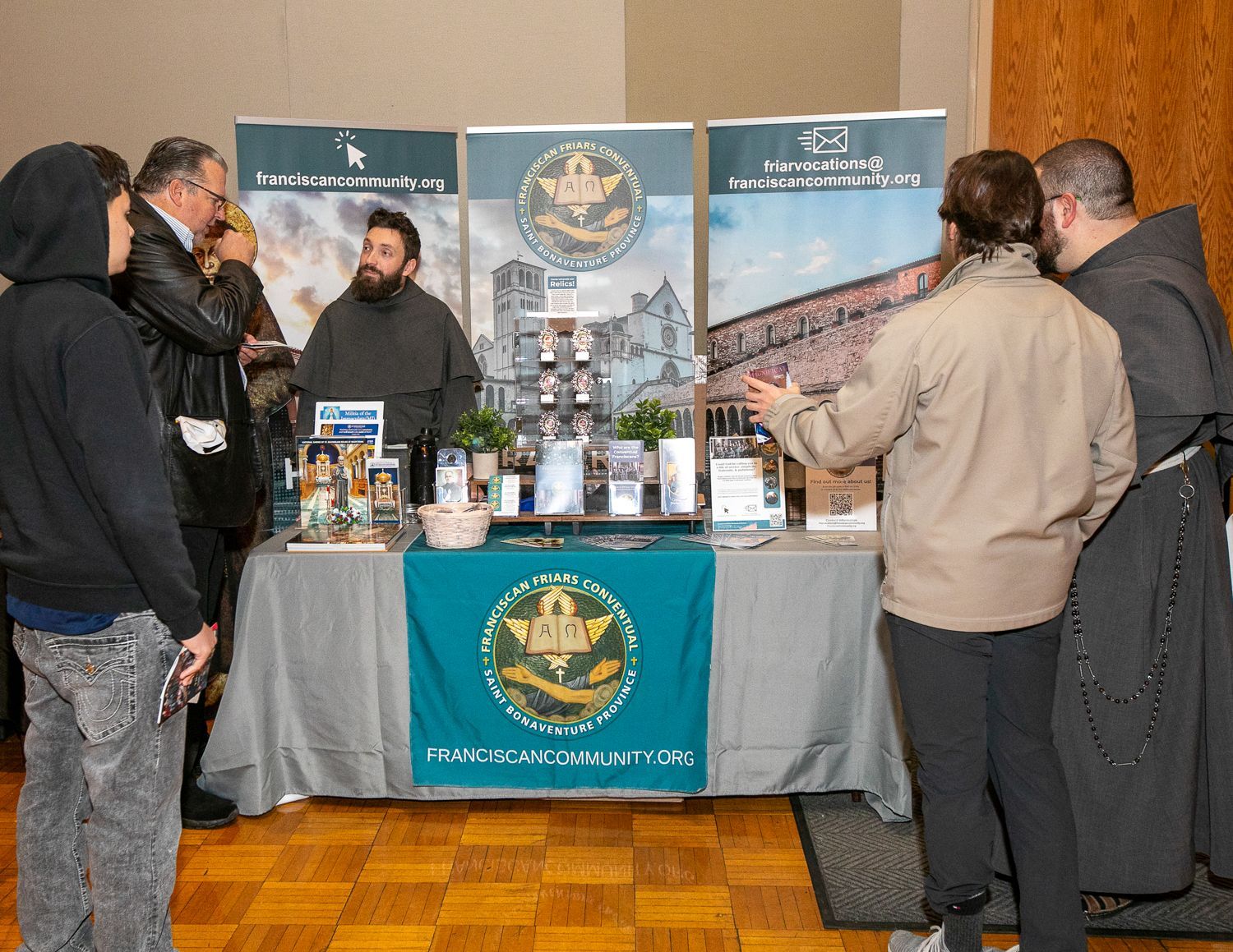 Trade booth with a teal-and-gold banner, brochures, and several people talking at a conference.