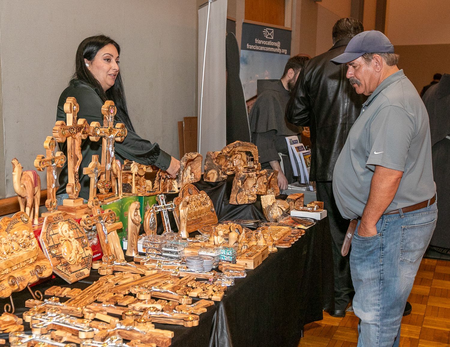 Vendor display of handcrafted wooden items at a market booth, with two shoppers examining the table.