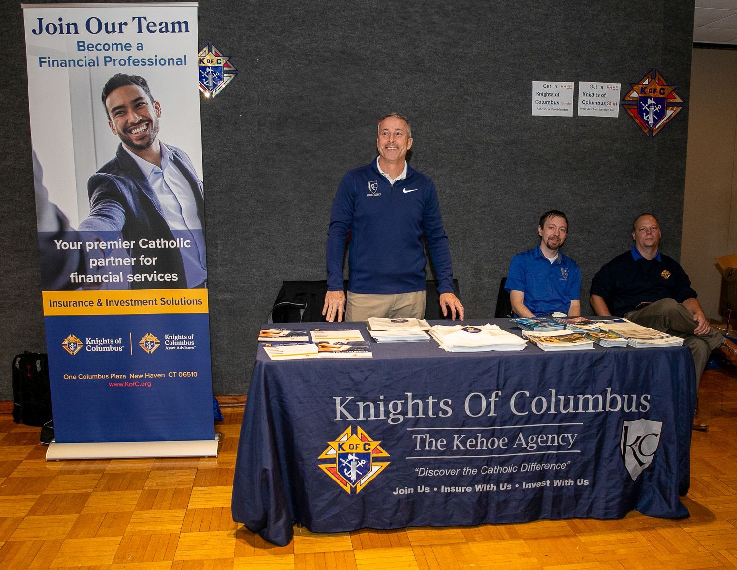 Three men at a Knights of Columbus table beside a 