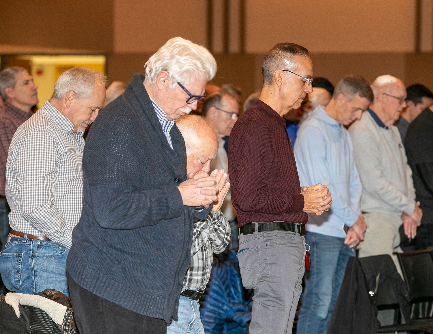 People standing in a quiet hall with heads bowed, as if in prayer or reflection.