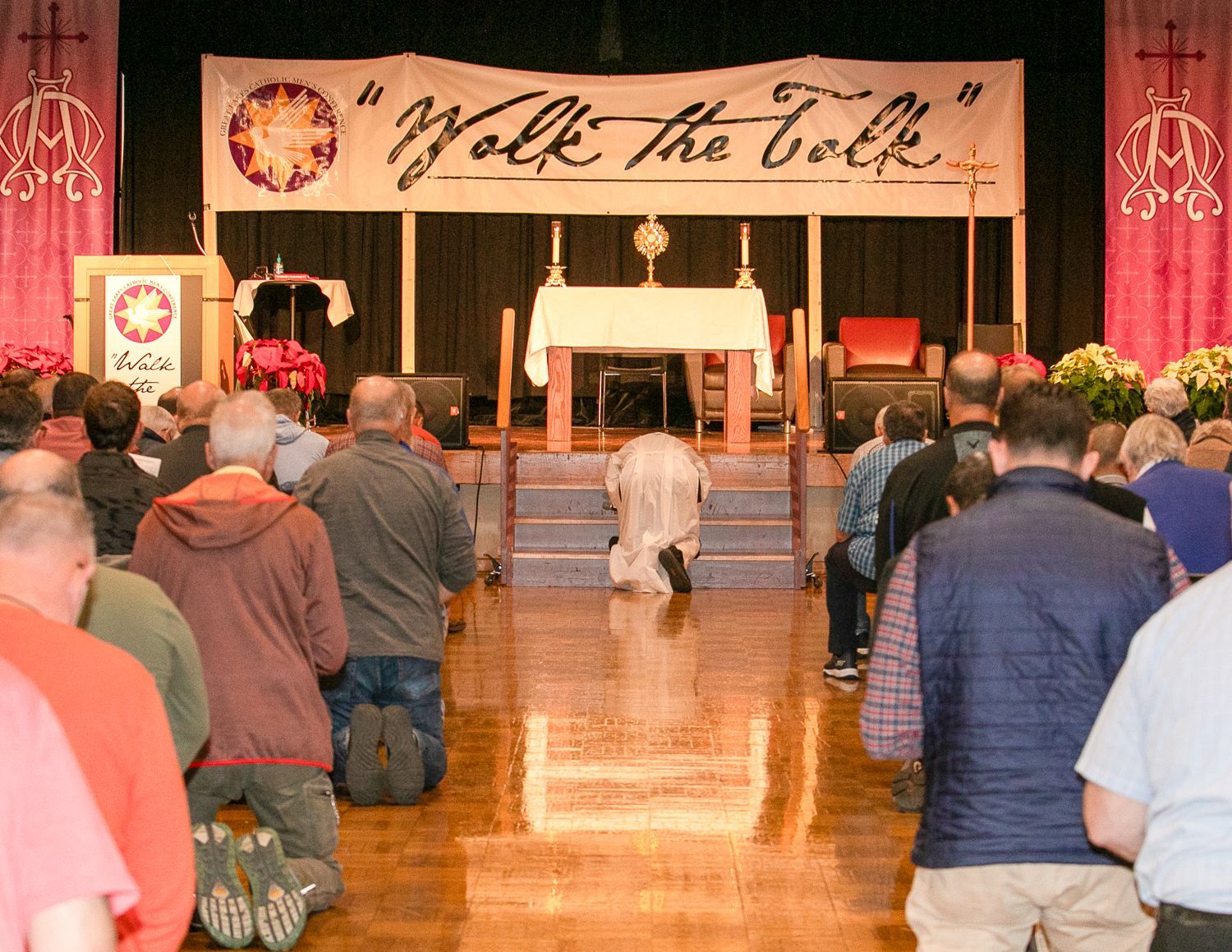 People kneeling in a church aisle facing an altar under a “Walk the Talk” banner