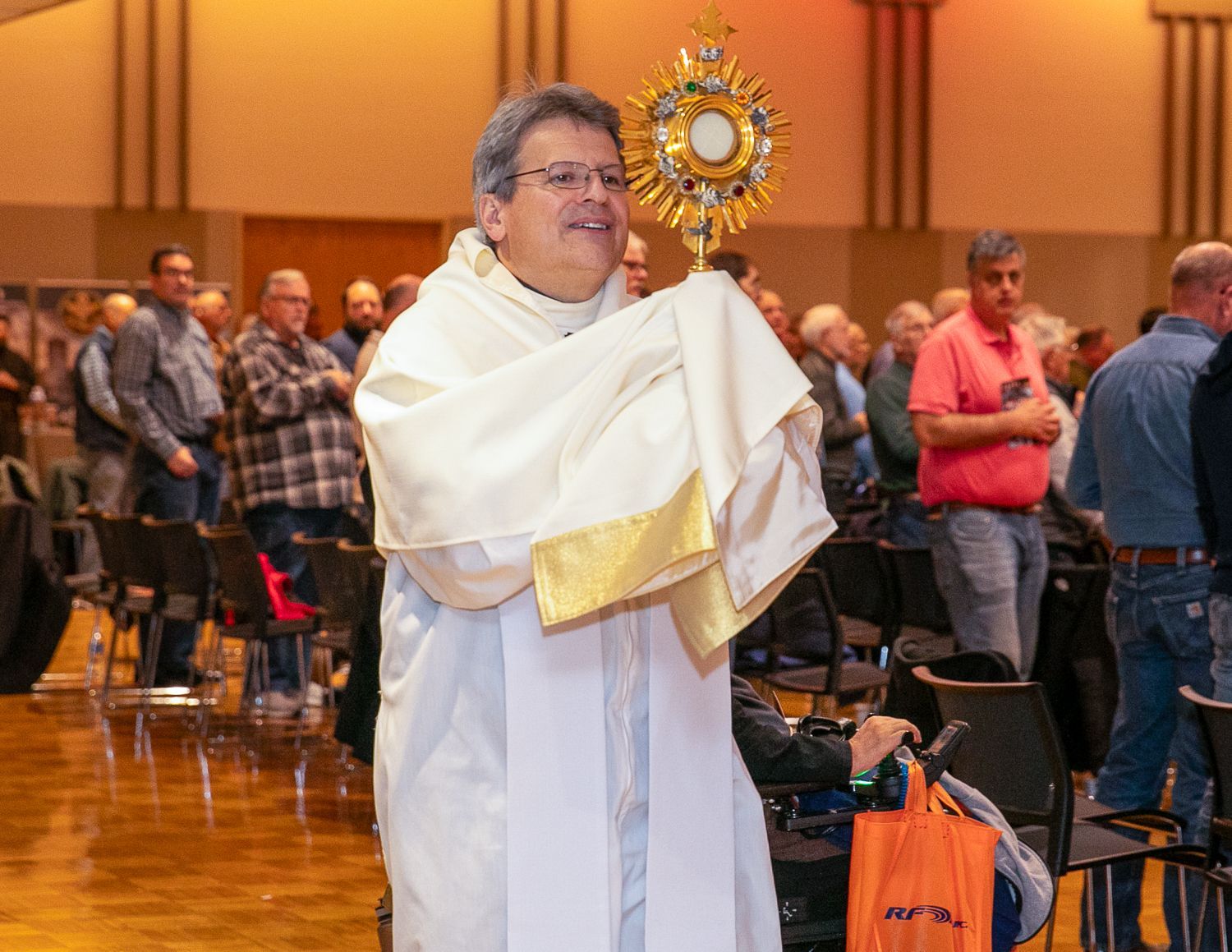 Priest in white vestments holding a golden monstrance during a church procession