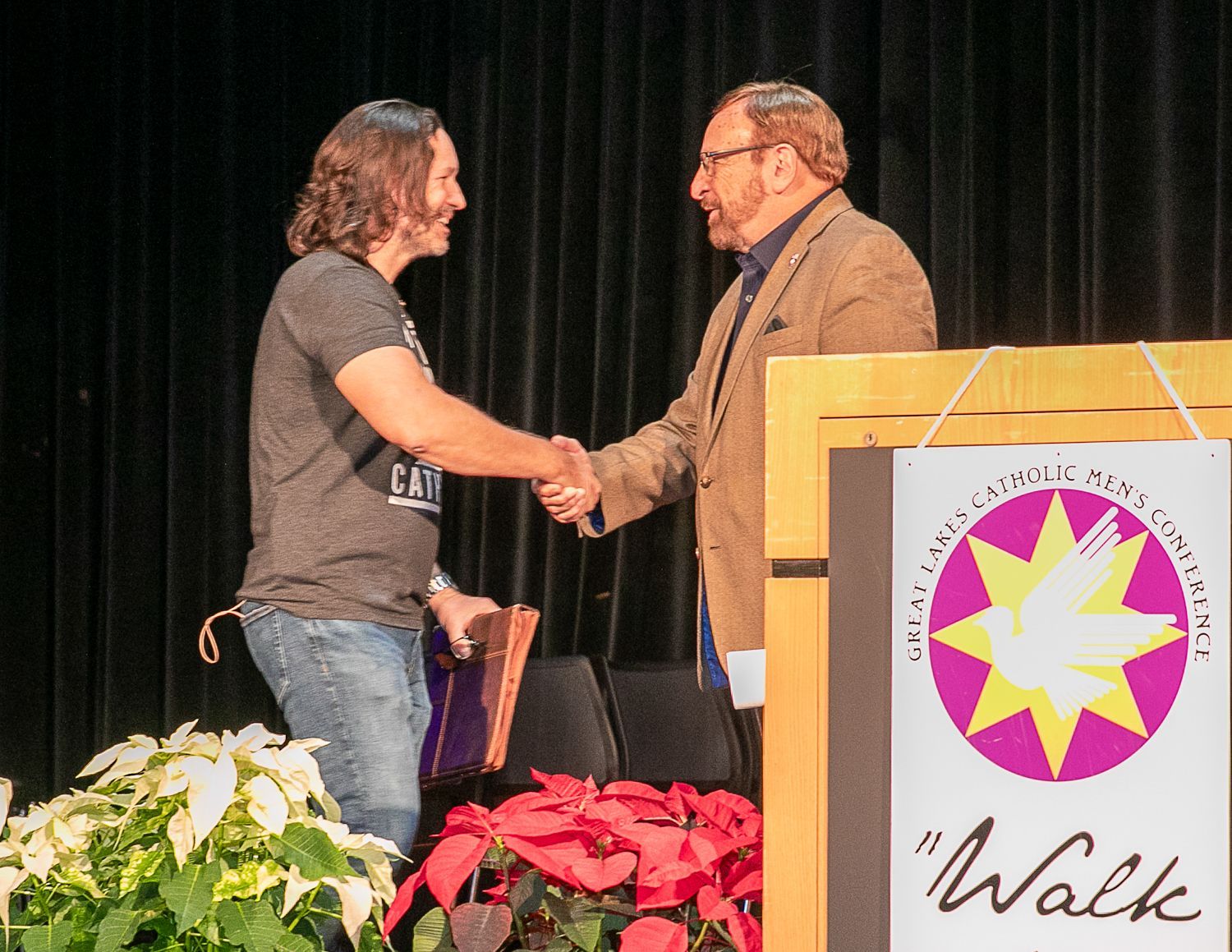 Wayne Messmer and Keith Nester shaking hands onstage beside a podium with a “Walk” sign and flowers