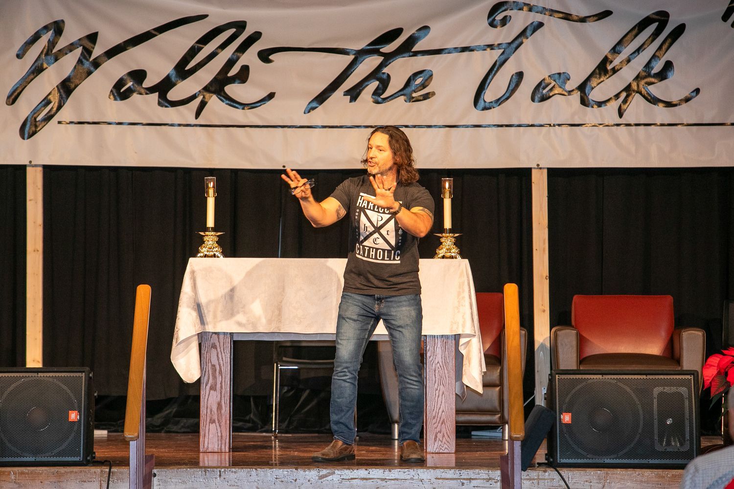 Keith Nester speaking at a church altar with a microphone, under a “Walk the Talk” banner.