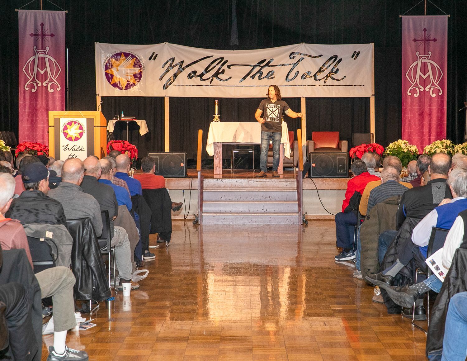 Keith Nester at podium on a stage facing an audience in an indoor hall with a 
