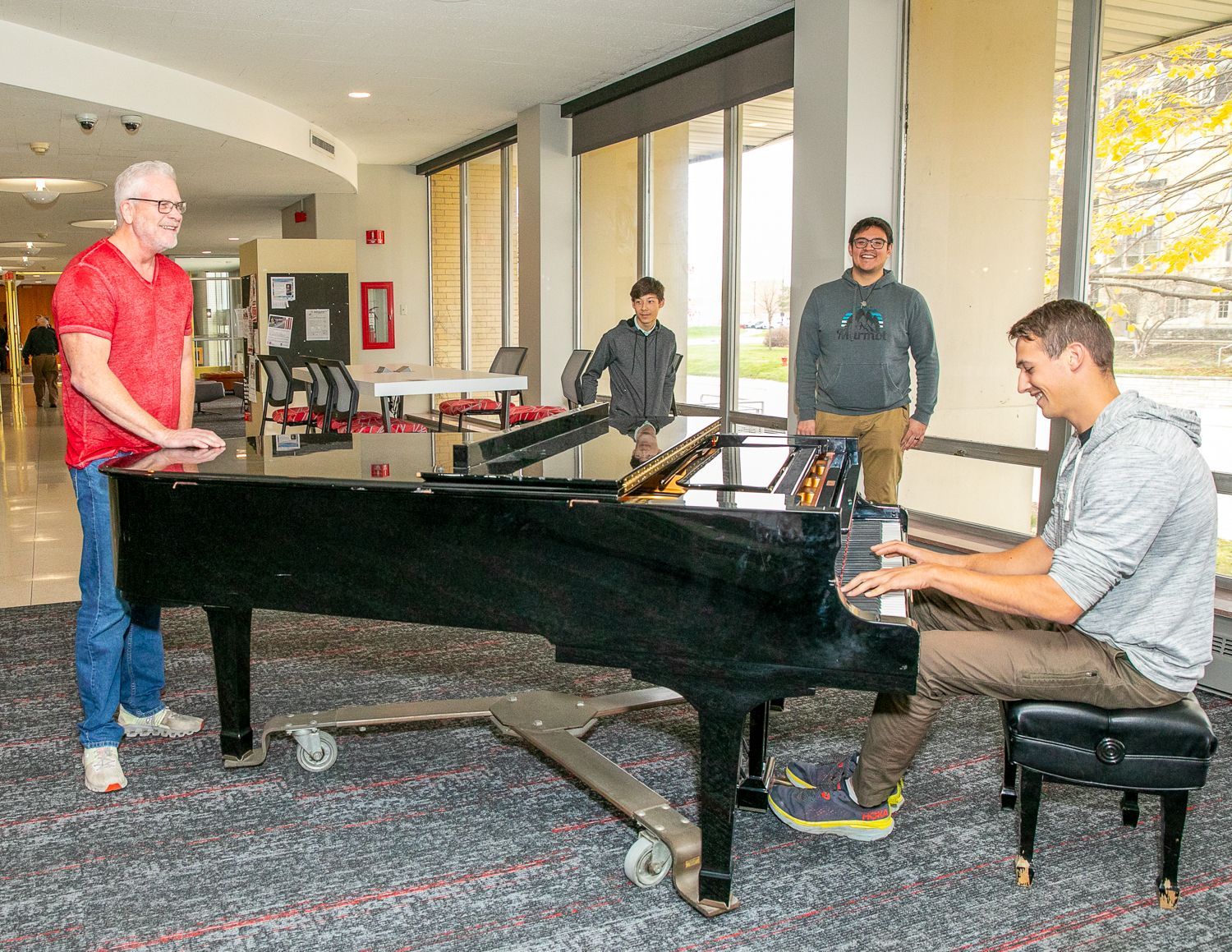 People gathered around a grand piano in a bright room, with one person seated and playing.