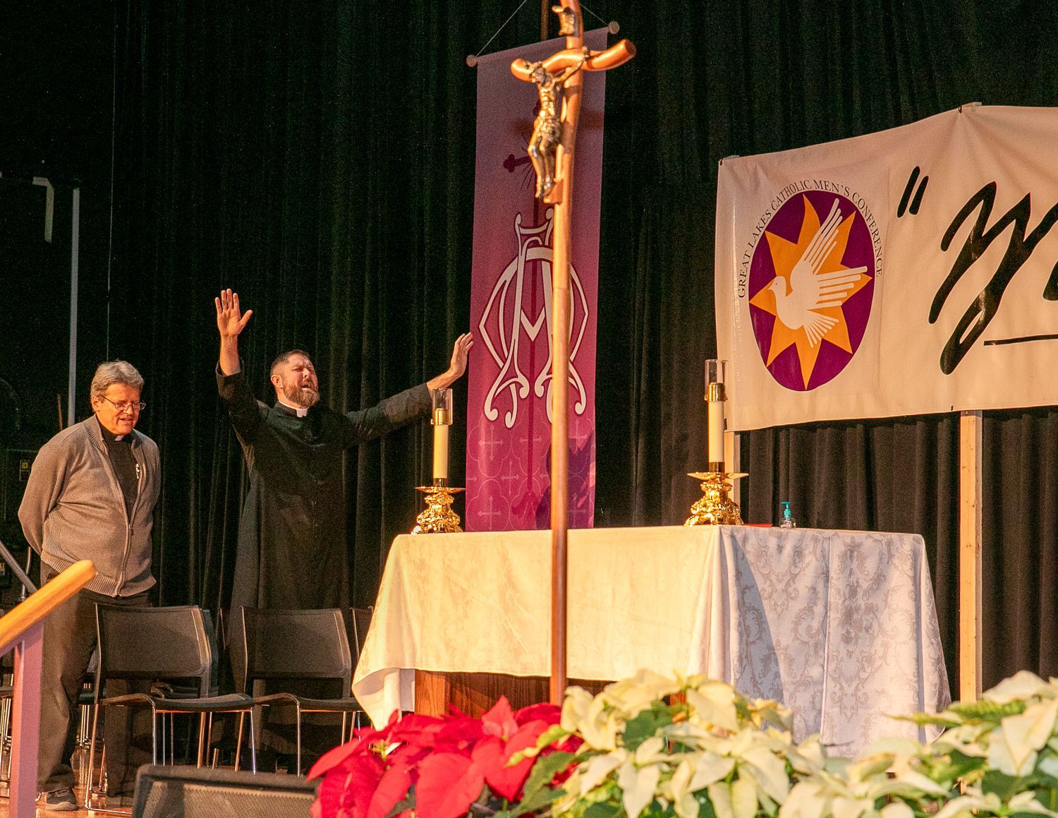 Two people on a church stage beside a large cross draped in purple and a white banner with a dove emblem.