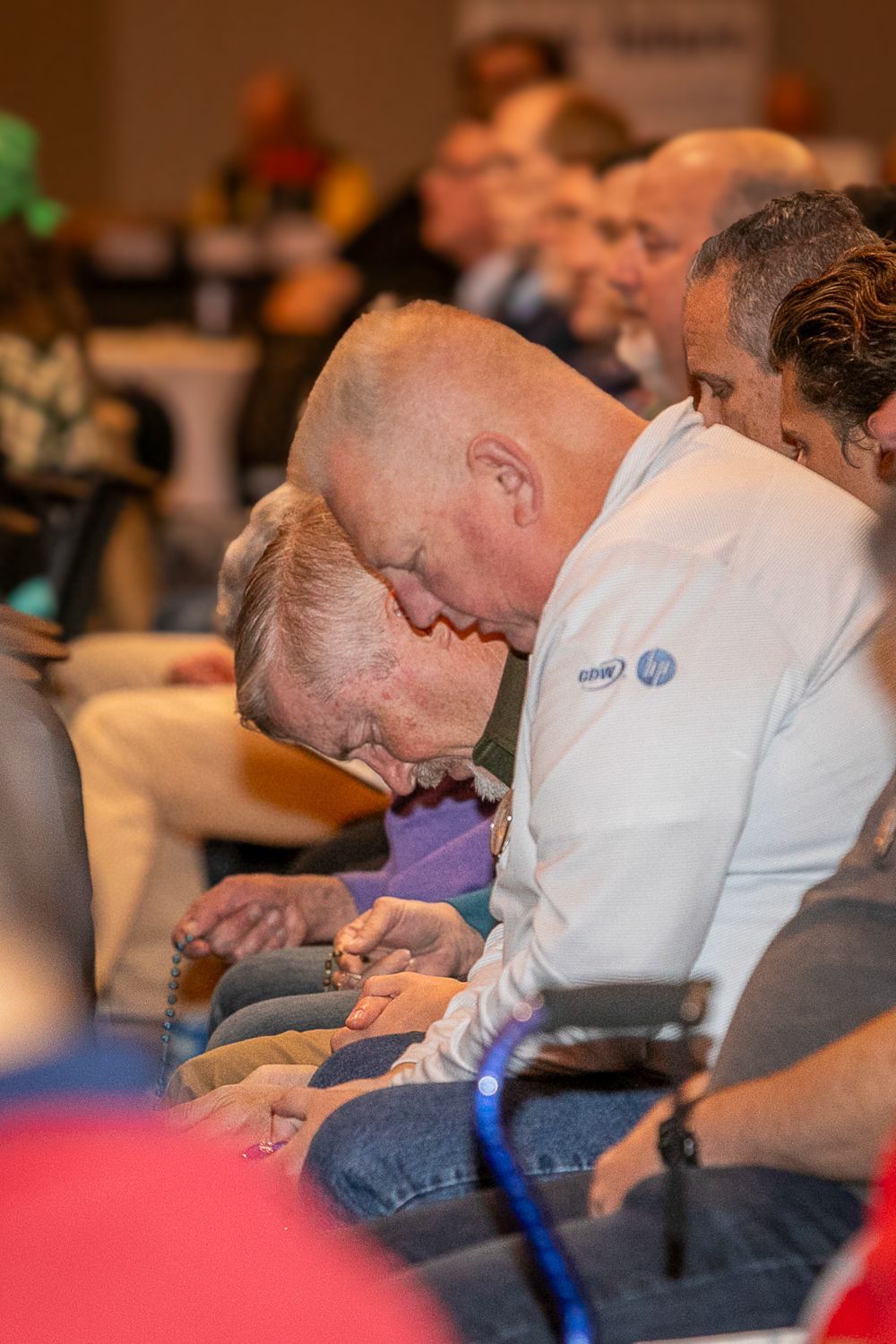 Audience members sitting with heads bowed, praying at a Catholic men's conference.