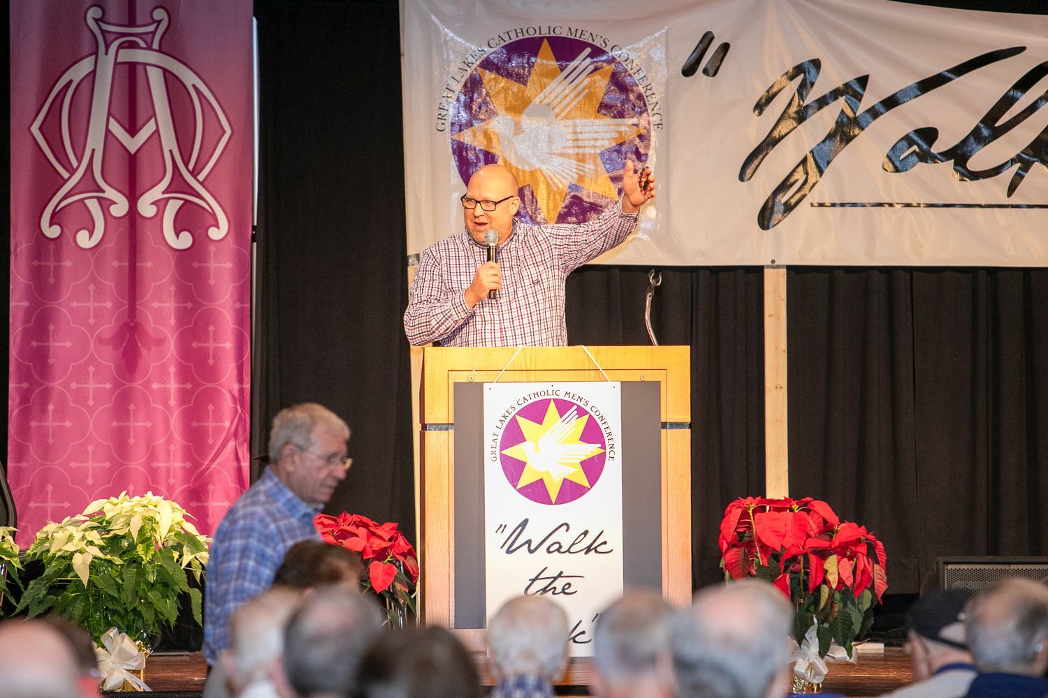Mitch Striedl speaking at a podium on stage with pink banners and floral decorations