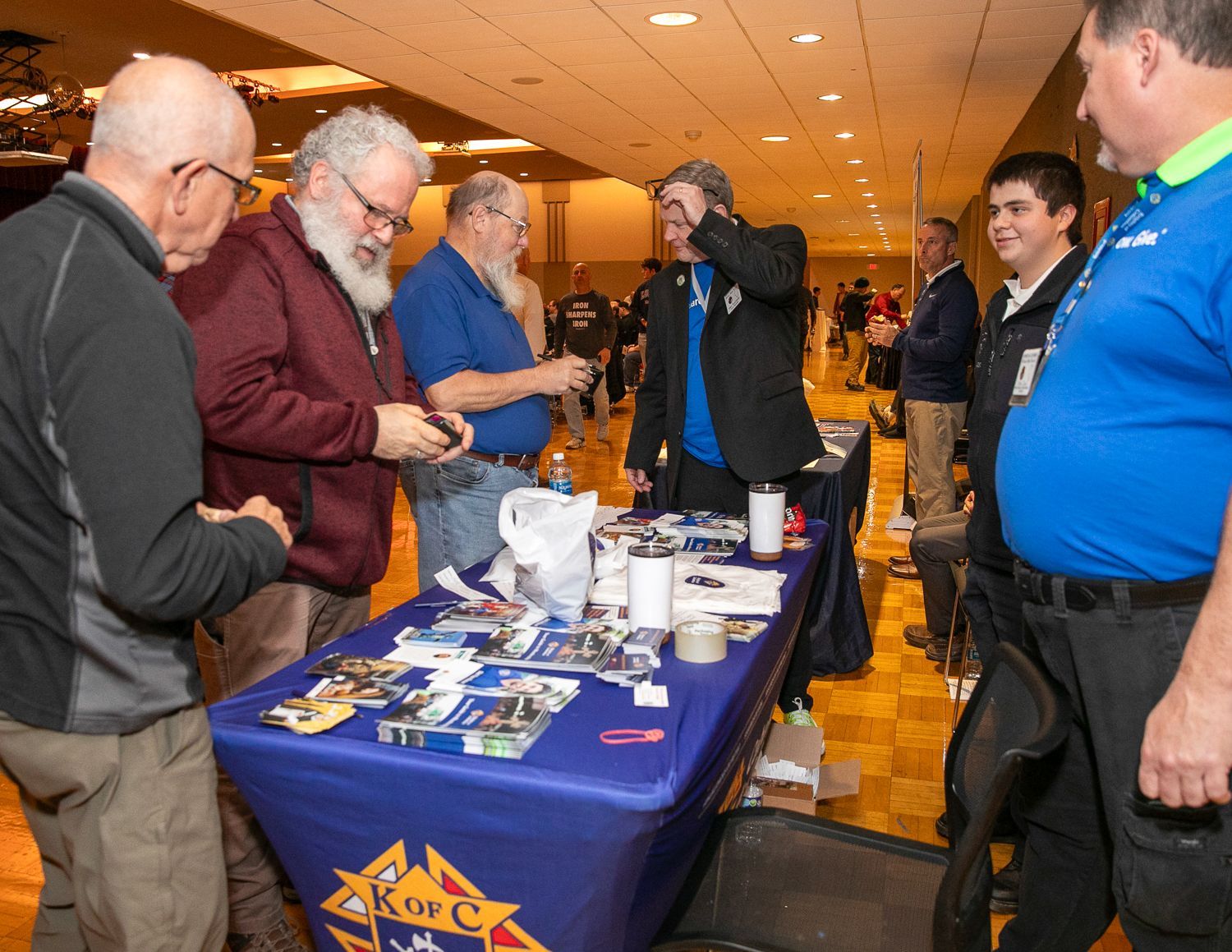 People at a convention table talking and browsing items under warm indoor lighting
