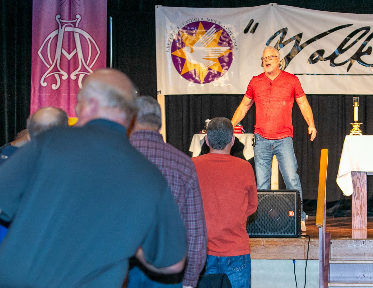 Sean Forrest in red shirt speaking on a stage to an audience in a hall