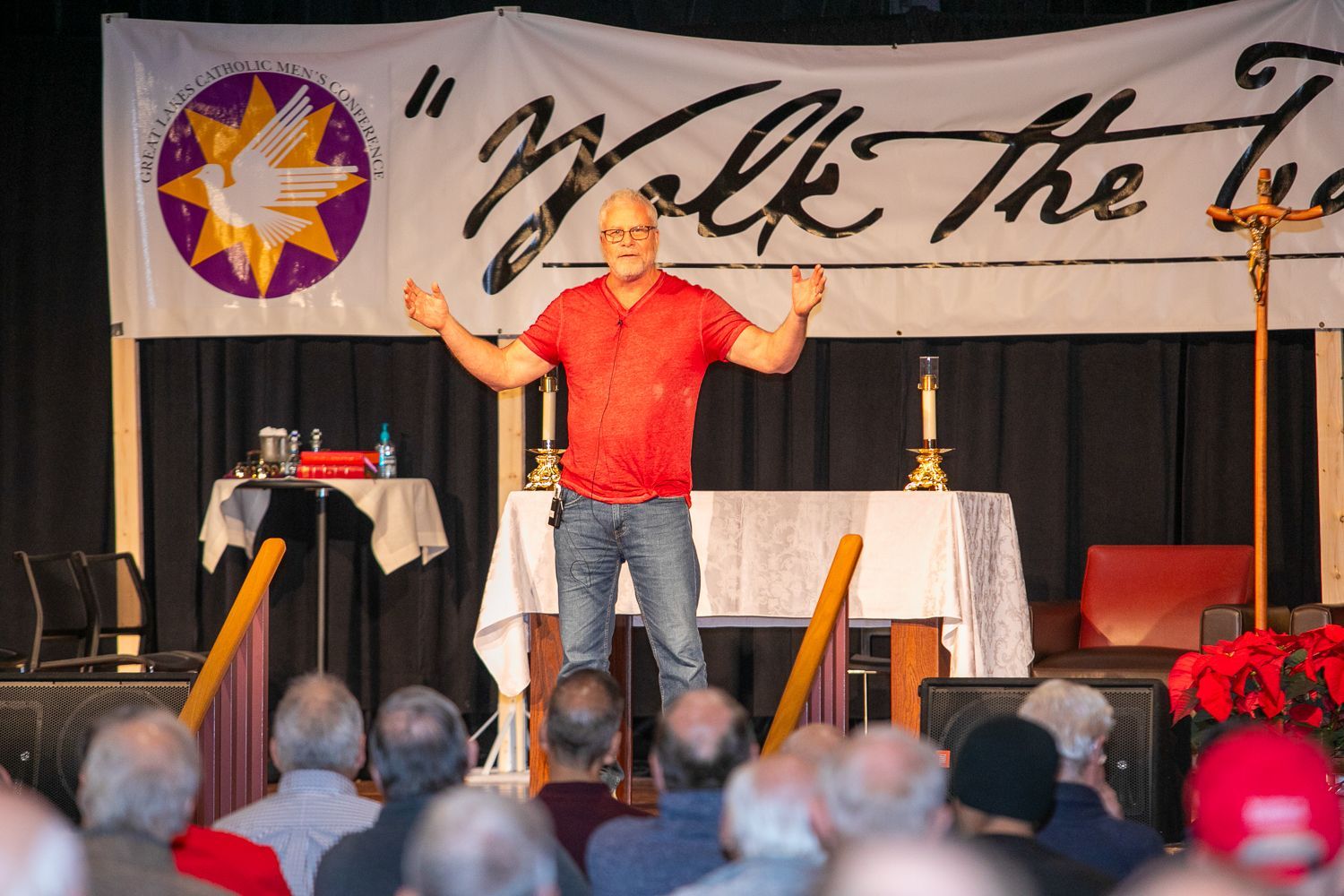 Sean Forrest in red shirt speaking on stage with arms raised before an audience