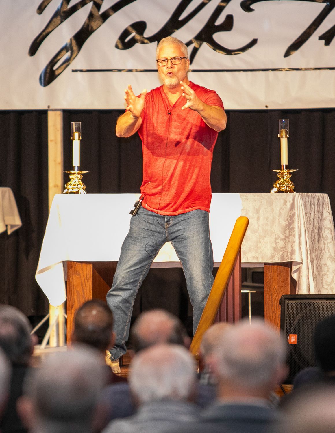 Sean Forrest in red shirt speaking on stage with audience in foreground