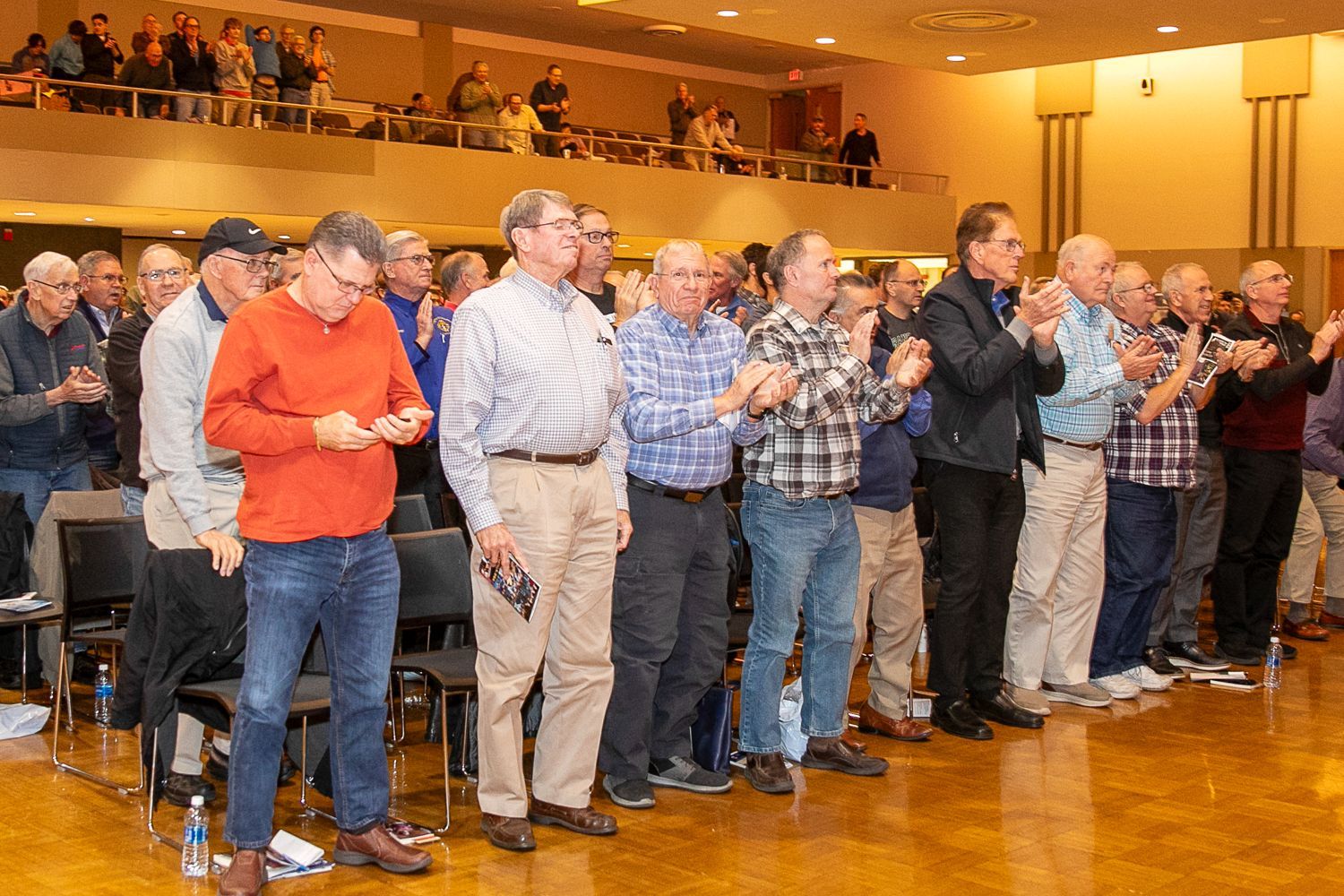 People standing and applauding in a conference hall with warm lighting