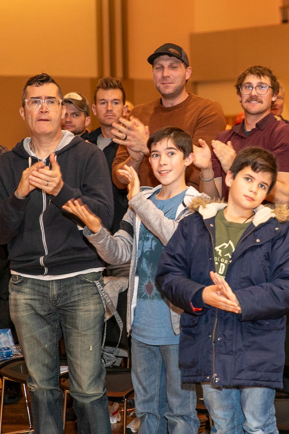 Group of people standing indoors, clapping and smiling in a warmly lit room
