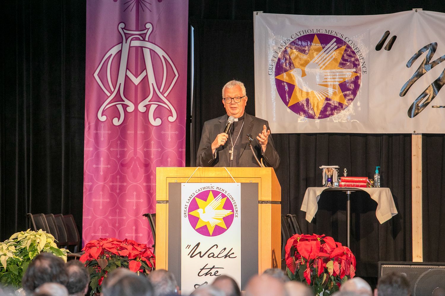 Speaker at podium on stage with purple and white banners and flowers in front