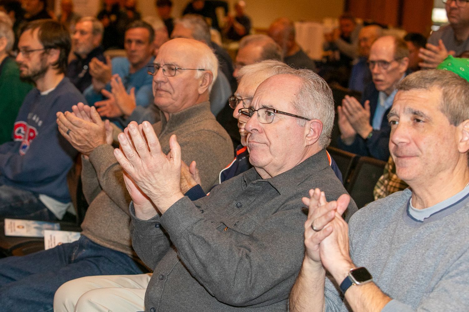 Audience members seated indoors, clapping and smiling during a presentation.