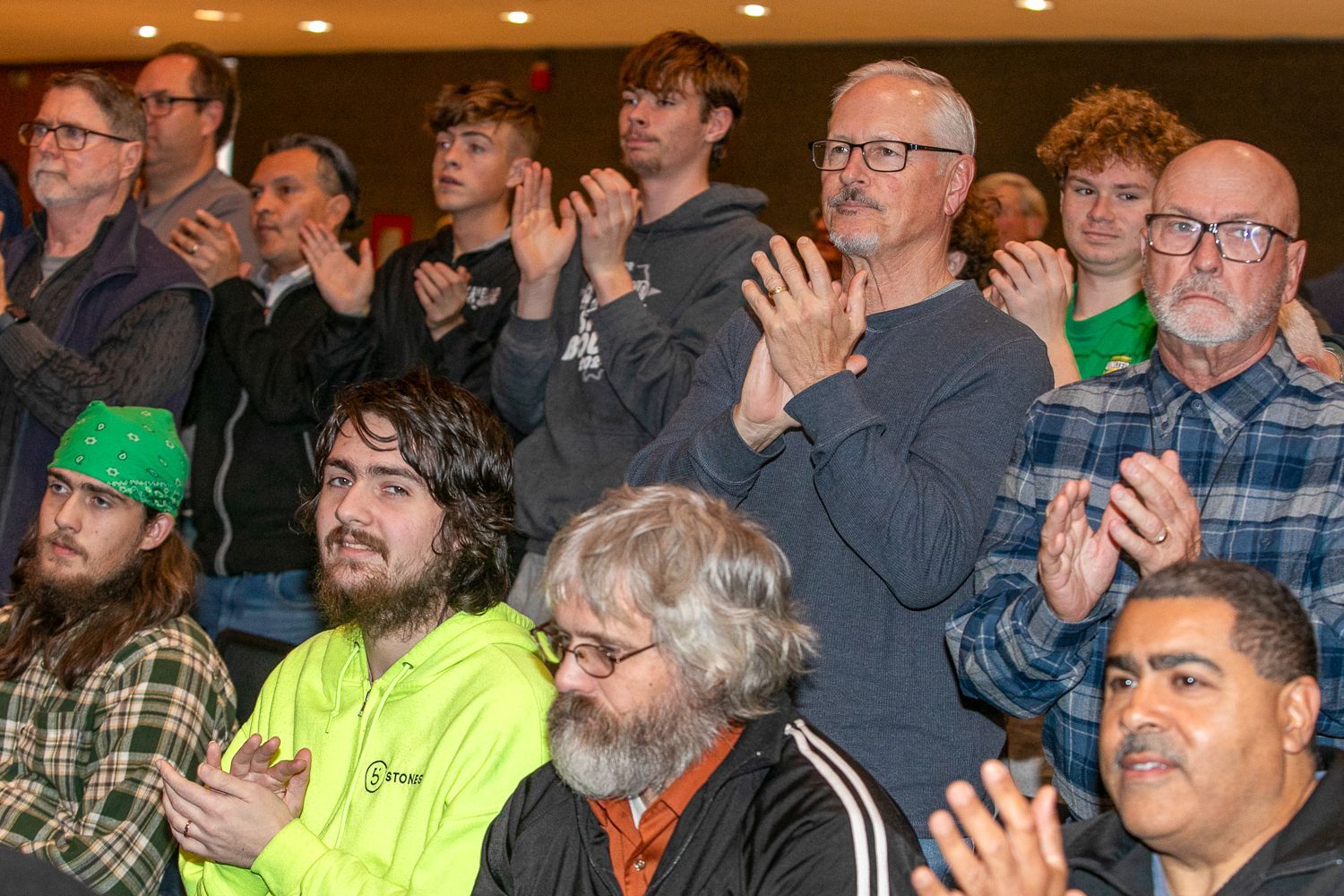 Audience applauding in a crowded indoor event, with several people smiling and clapping.