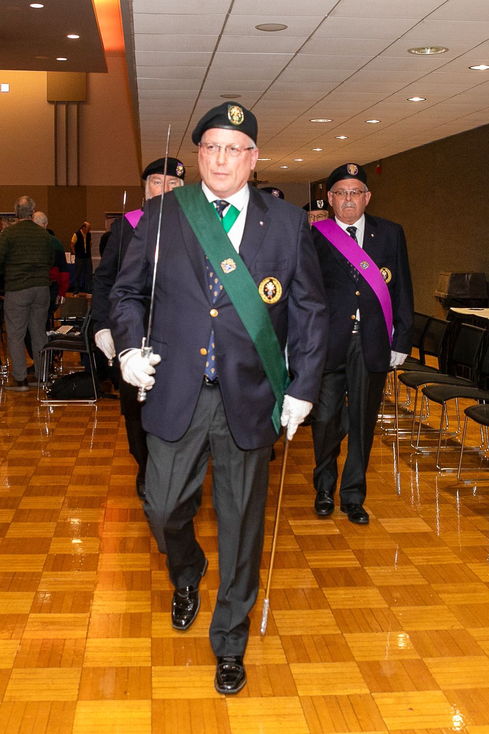 Two uniformed men with sashes walking down a hall with parquet flooring