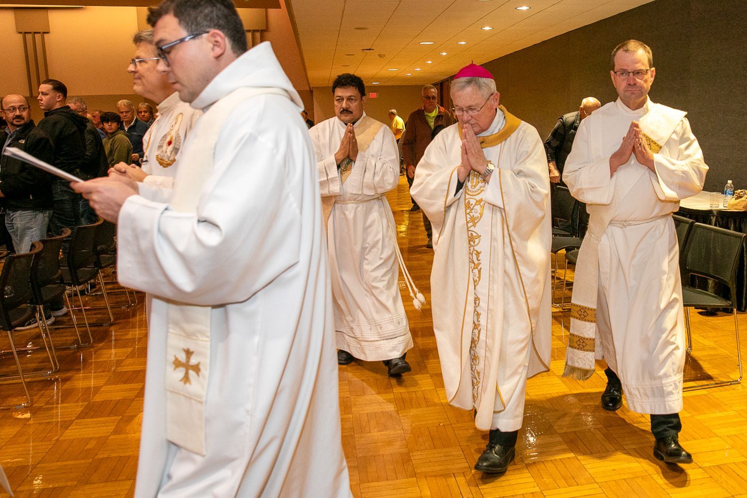 Clergy in white robes process through a church hall during a religious ceremony