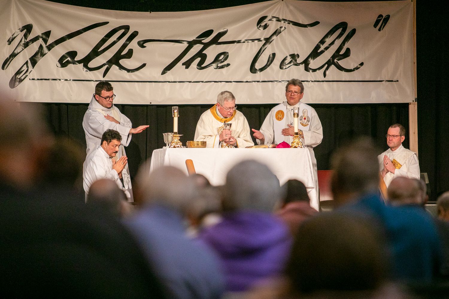 Panel discussion on a stage under a “Talk the talk” banner, with speakers seated at a table and an audience in front.