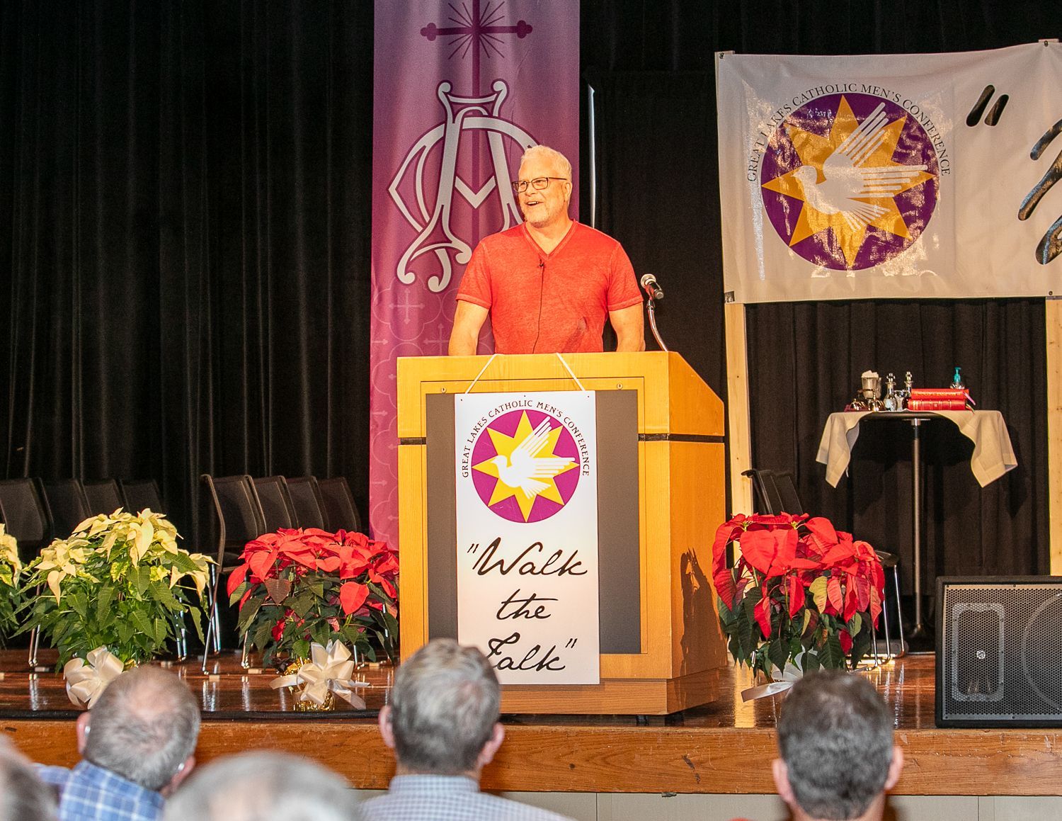 Sean Forrest at podium on stage with floral decorations and audience heads in foreground