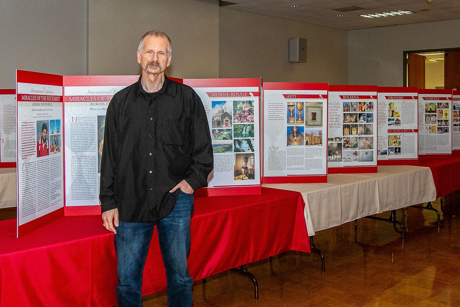 Man standing beside the International Exhibition of the Eucharistic Miracles of the World at a Catholic men's conference.